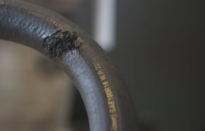 A burst rubber hydraulic hose that needs replaced