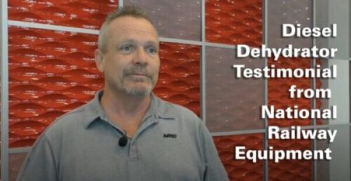 Man smiling in front of red and grey wall with text overlay of Diesel Dehydrator Testimonial from National Railway Equipment